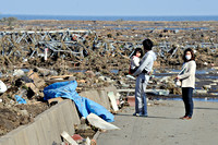 Twee volwassenen en een kind staren naar ravage van de tsunami